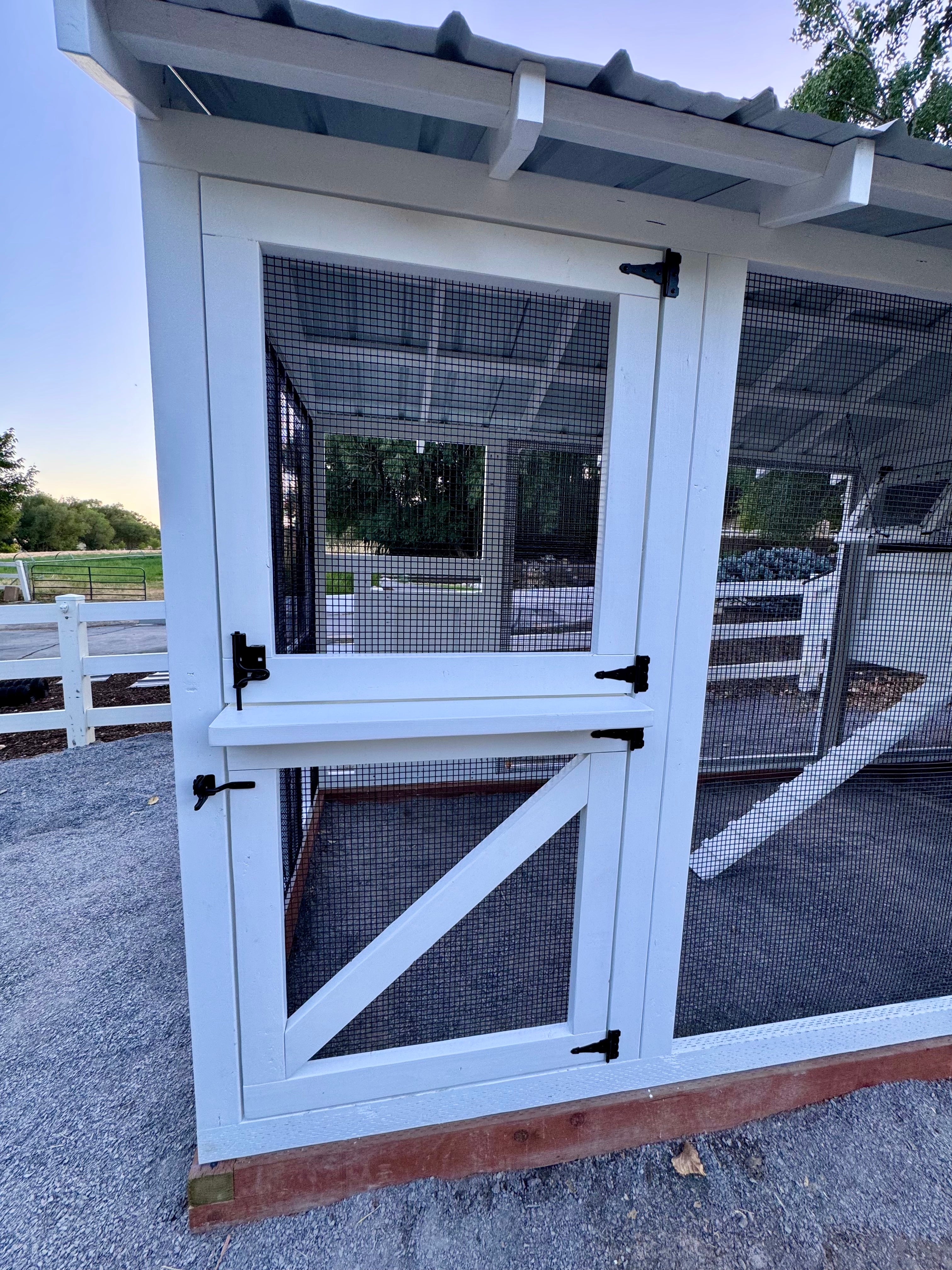A forwarding-looking view of a Dutch door found on a luxury chicken coop finished in a premium, white stain and black hardware throughout to accent tastefully.